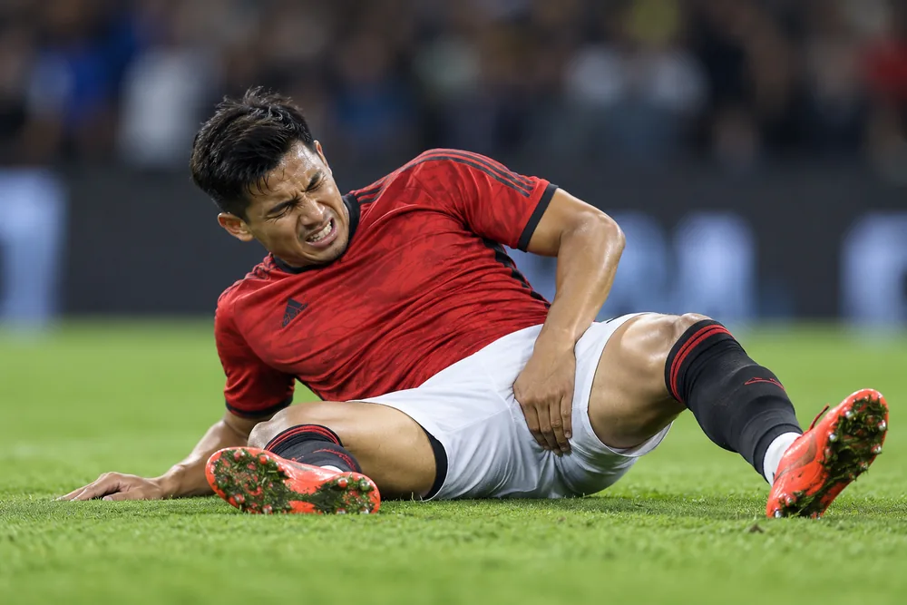 A football player sitting on the pitch and holding the right groin area after an injury